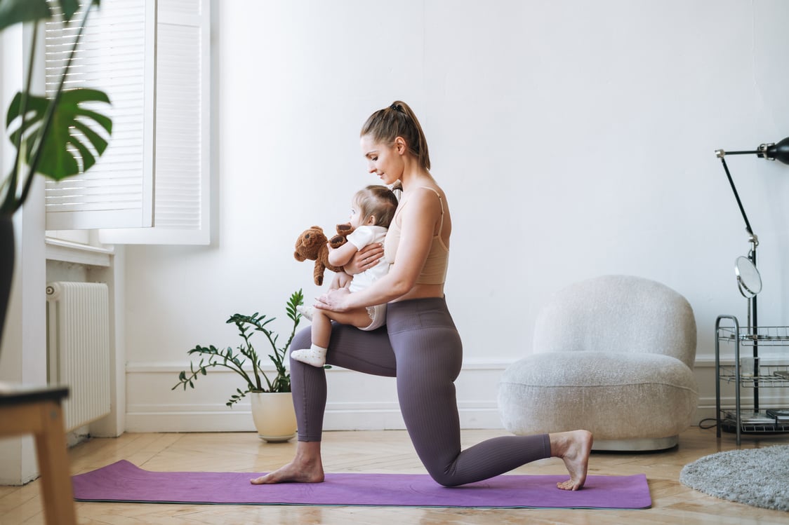 Young woman fit mom with baby girl in her arms doing fitness on